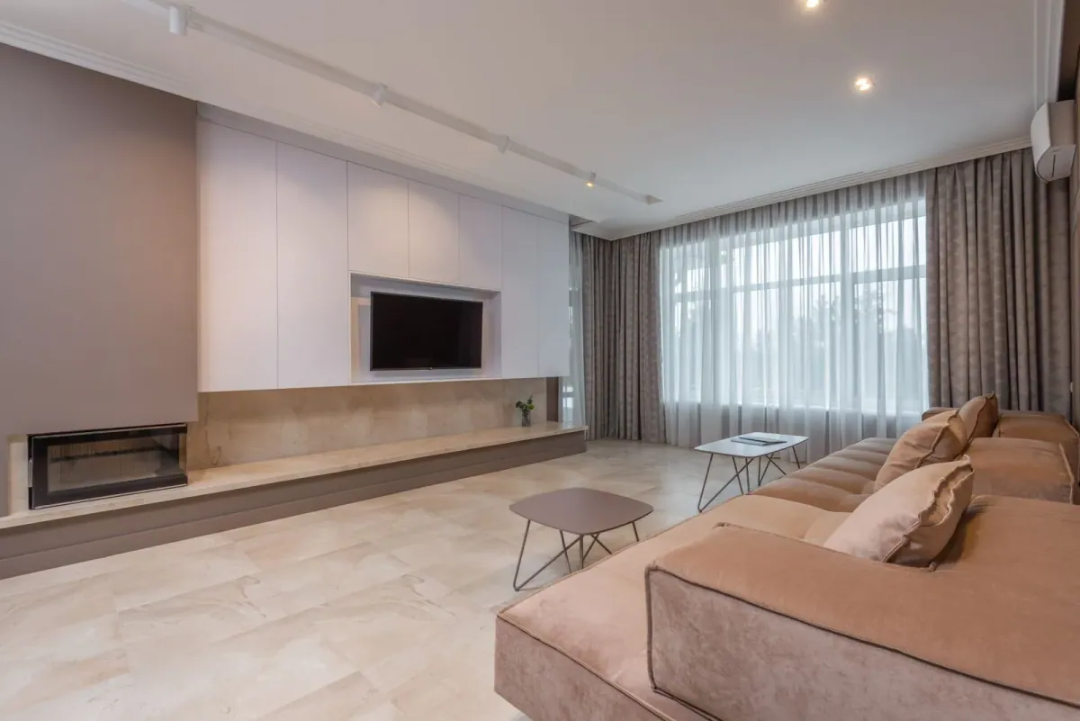 Großzügiger Wohnbereich mit beigem Sofa und breiter Fensterfront – Beispielmotiv