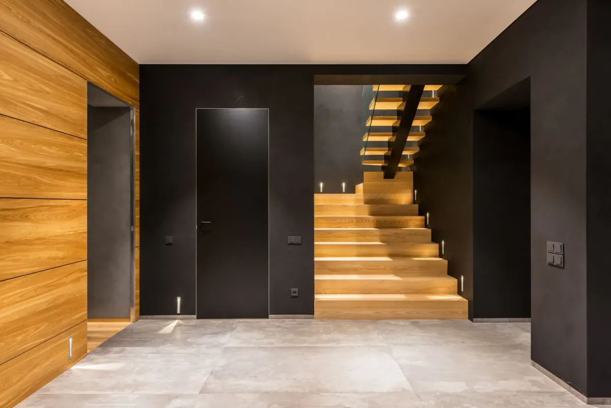 Holztreppe zwischen dunklen Wänden und hellem Steinboden – Wohninspiration